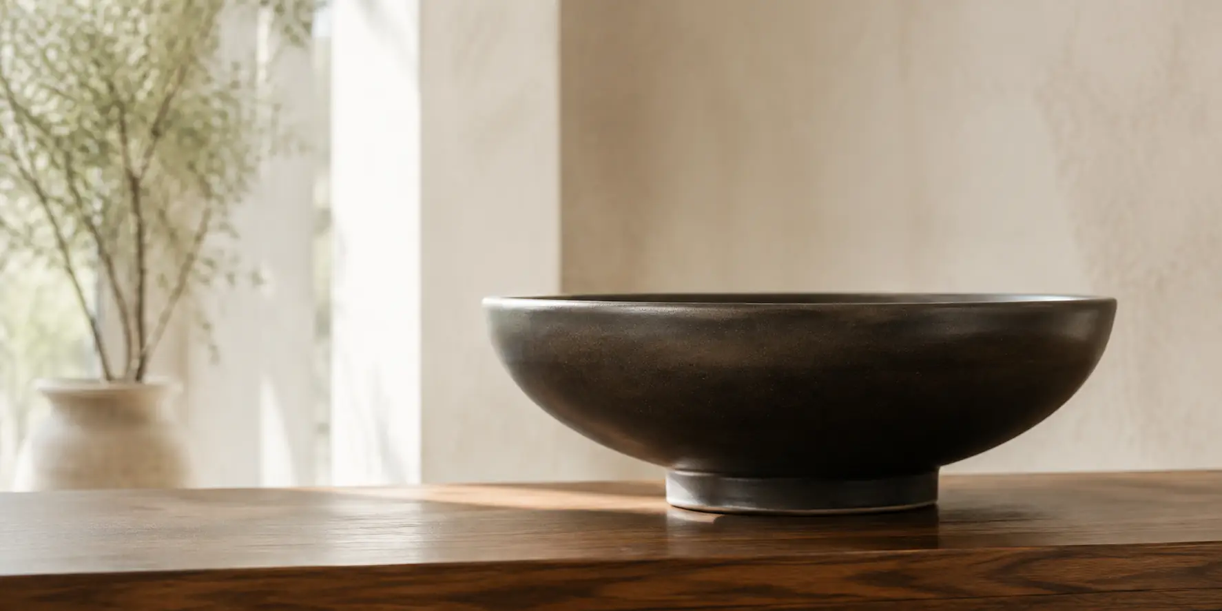 Hand-thrown dark ceramic bowl on walnut in natural daylight